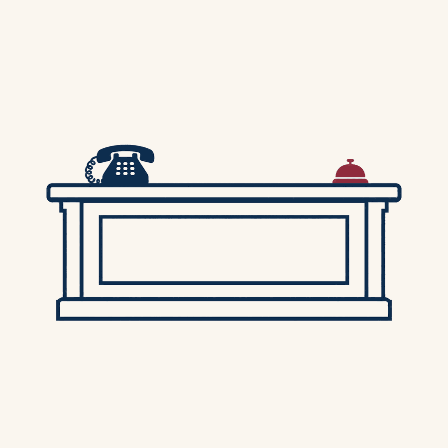A front desk counter with a telephone on one side and a burgundy desk bell on the other, illustrating the front desk coordinator's workstation